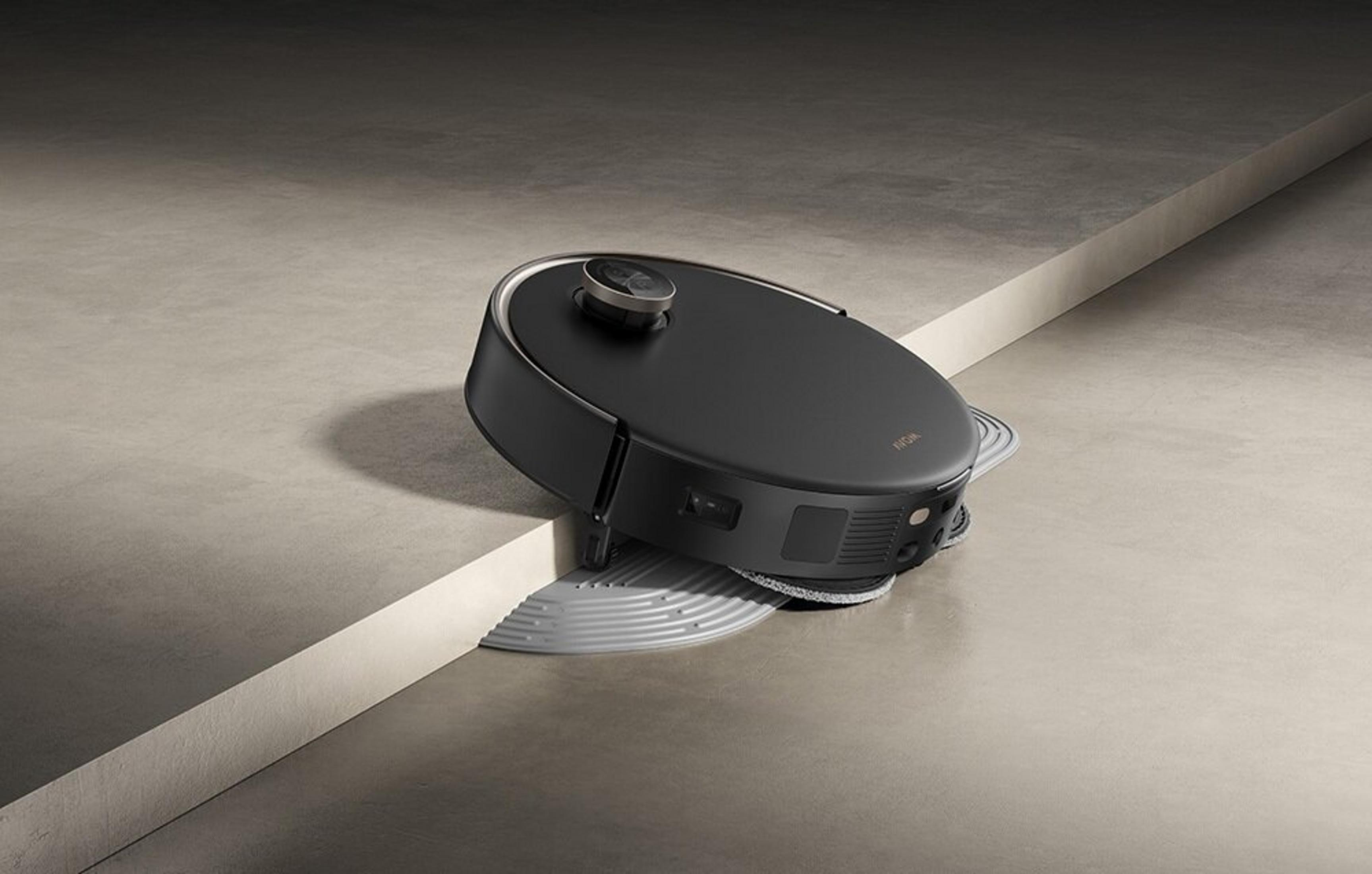 Czarny robot sprzątający porusza się po szarej podłodze podzielonej białym krawężnikiem.