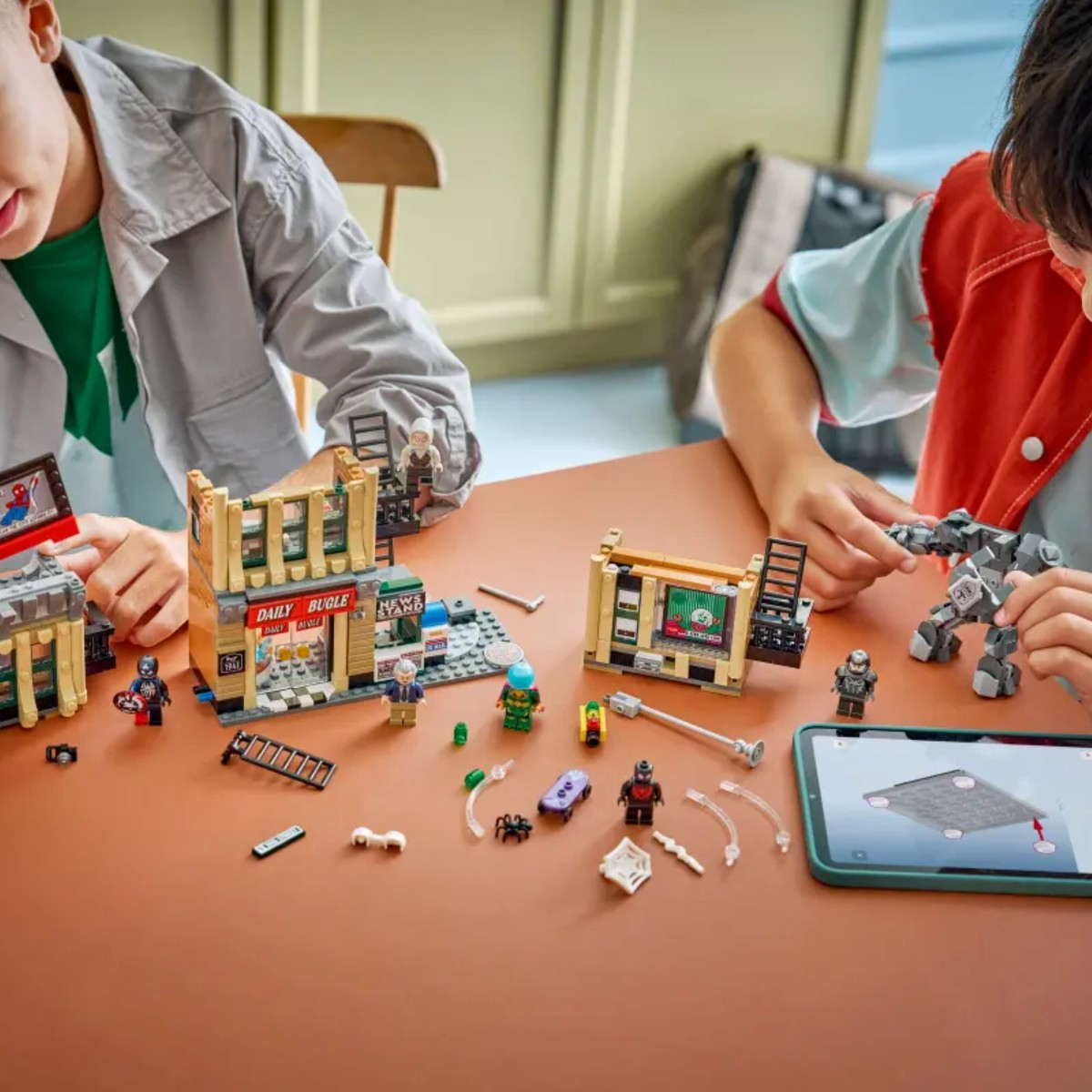 Dzieci budują zestaw Lego z figurkami Spidermana i kioskiem.