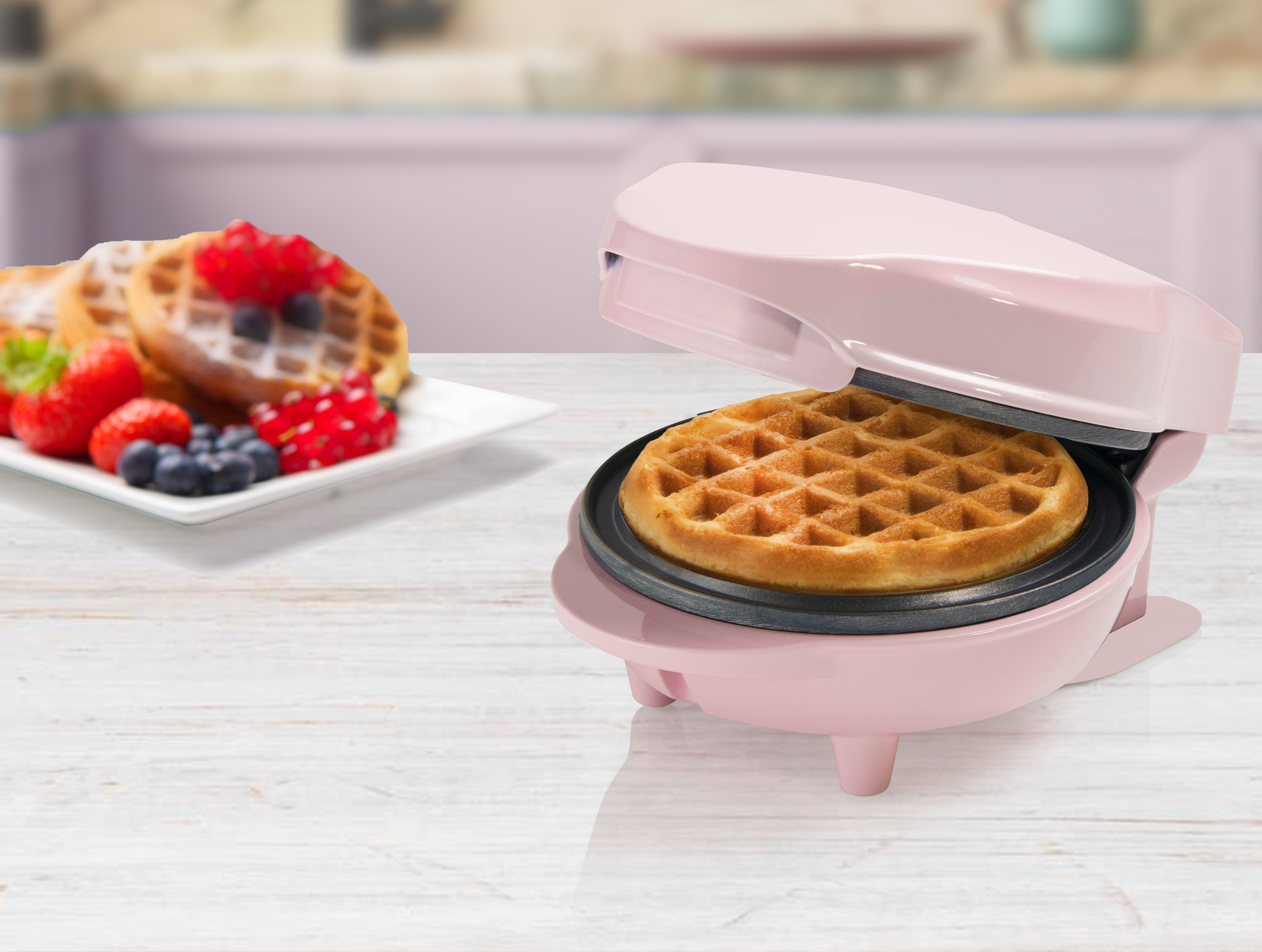 Ein rosa Waffeleisen mit einem fertigen Waffel und Beeren auf einem Teller.