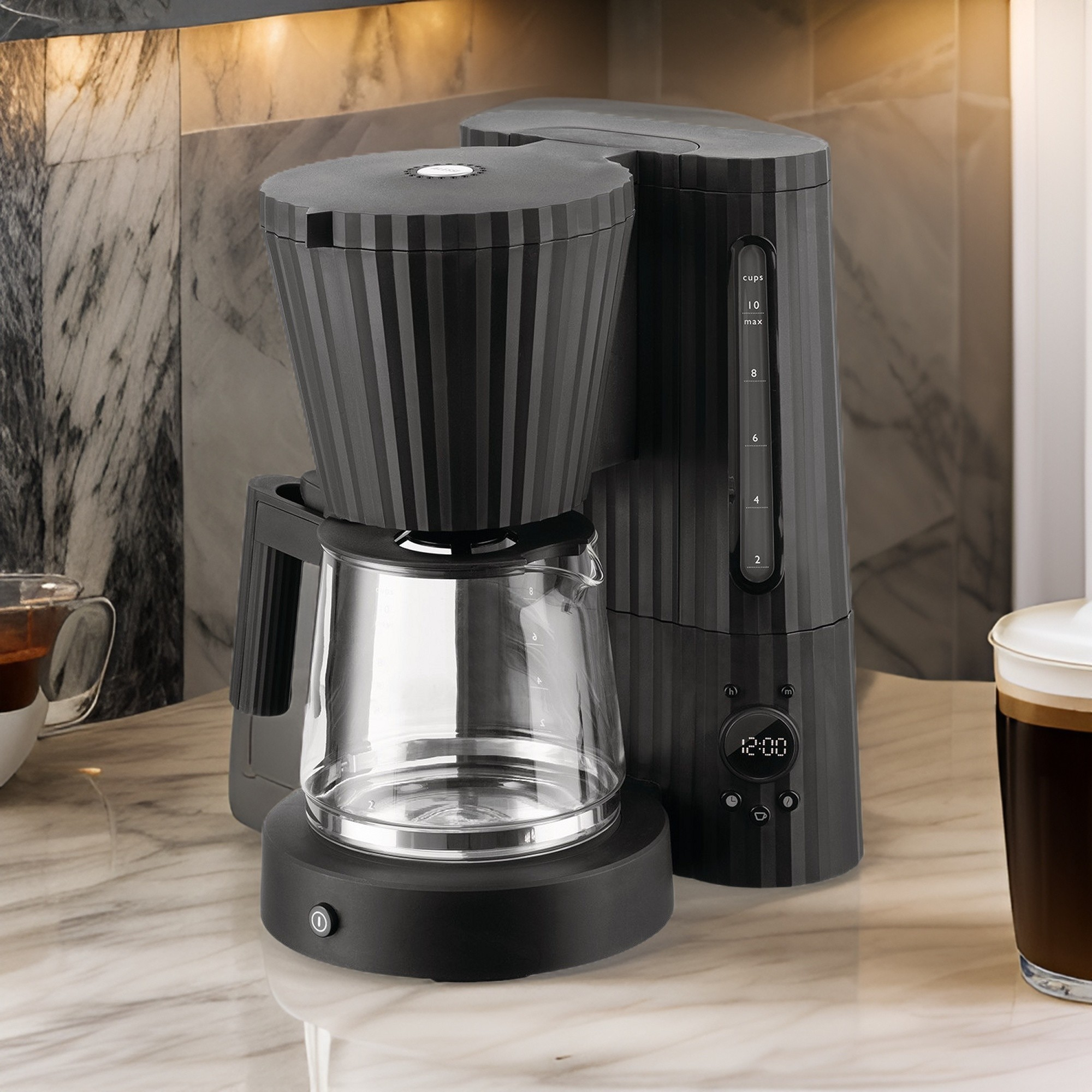 Macchina da caffè nera con caraffa in vetro su un piano di lavoro in marmo, accanto a una tazza di caffè.