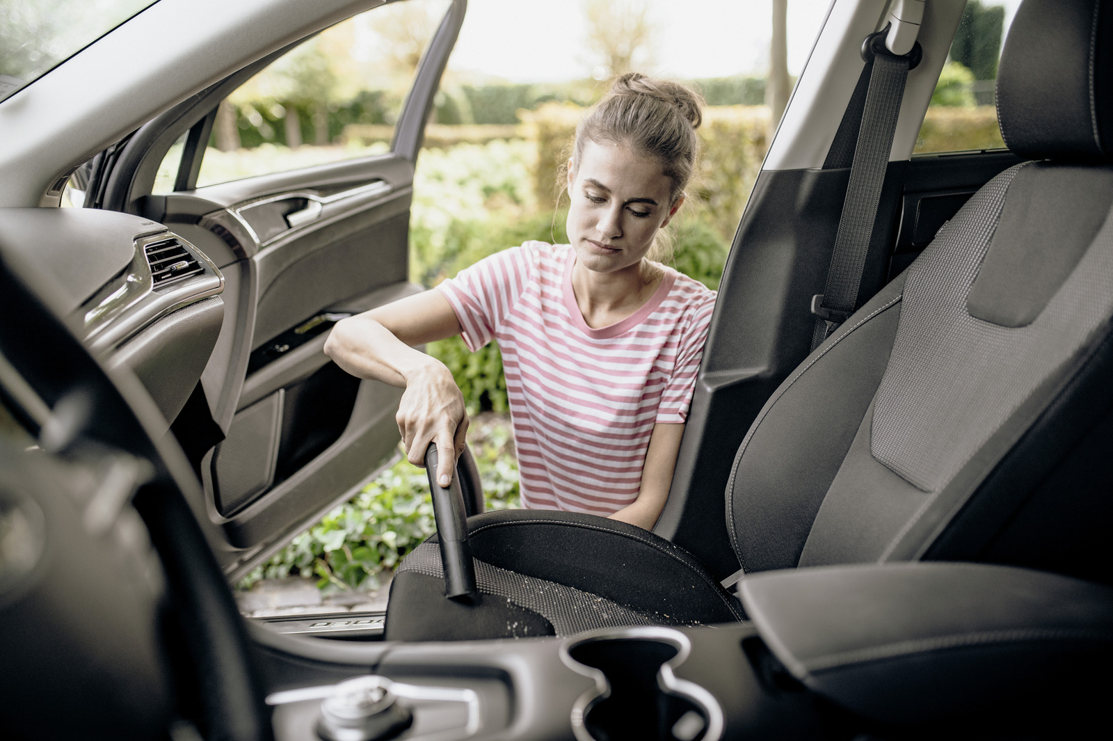 A woman vacuums the interior of a car.