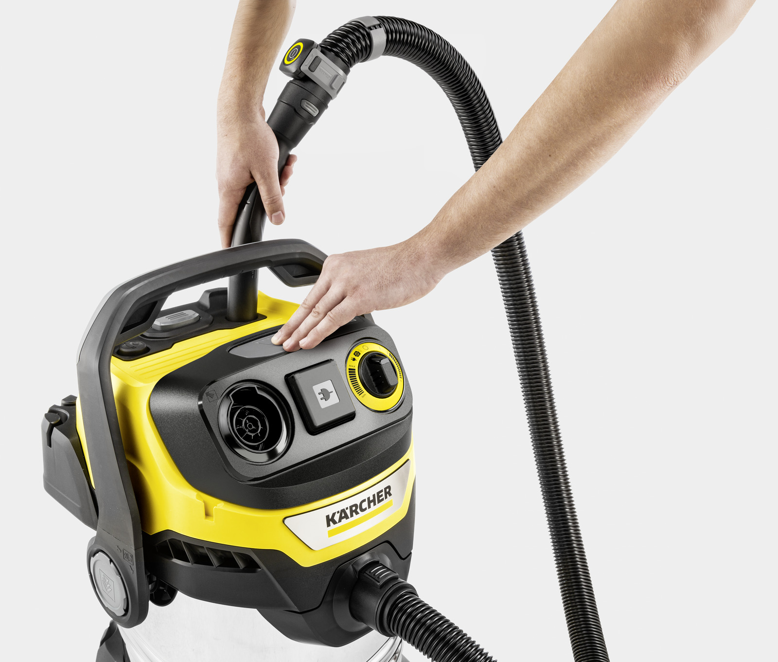 Hands connect hose to yellow and black Kärcher vacuum cleaner on a gray background.