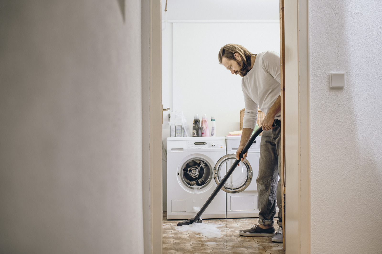 Een man zuigt schuim van de vloer in een wasruimte met een wasmachine.
