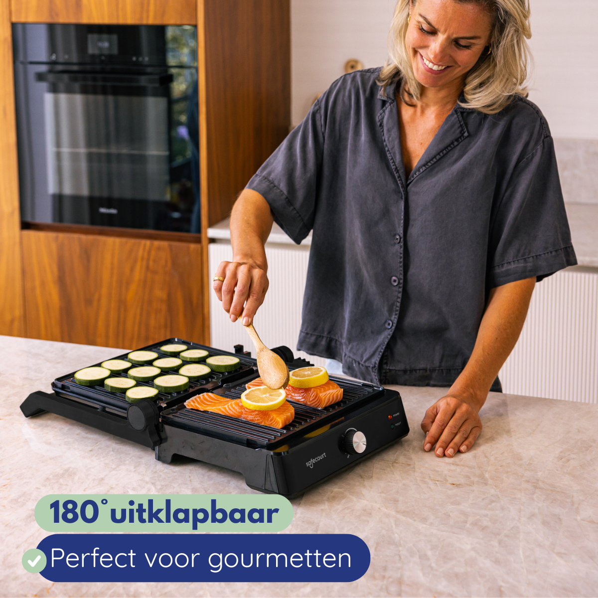 A woman grills salmon and zucchini on a tabletop grill using a wooden spatula.