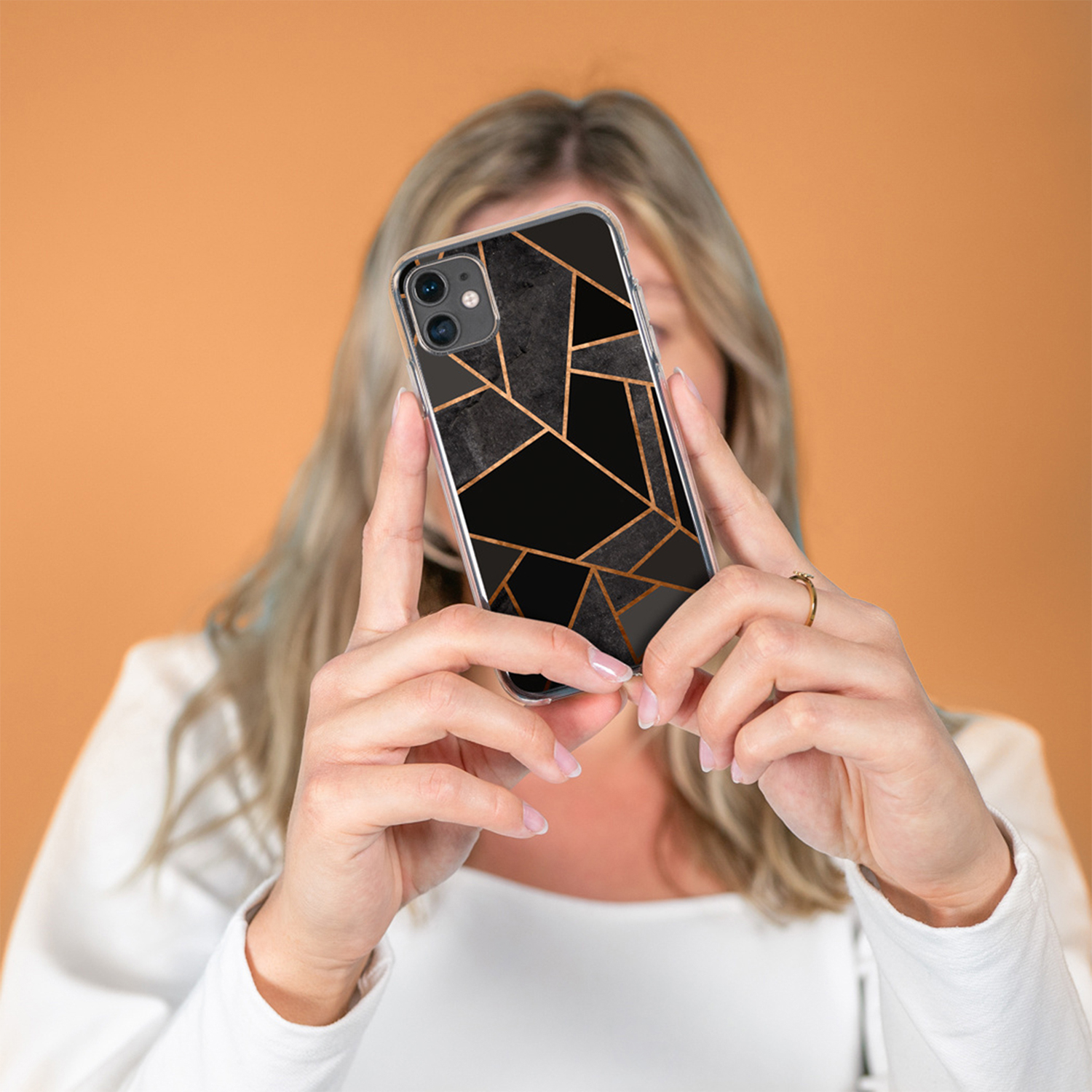 Una donna tiene uno smartphone con motivo di marmo nero e linee dorate.