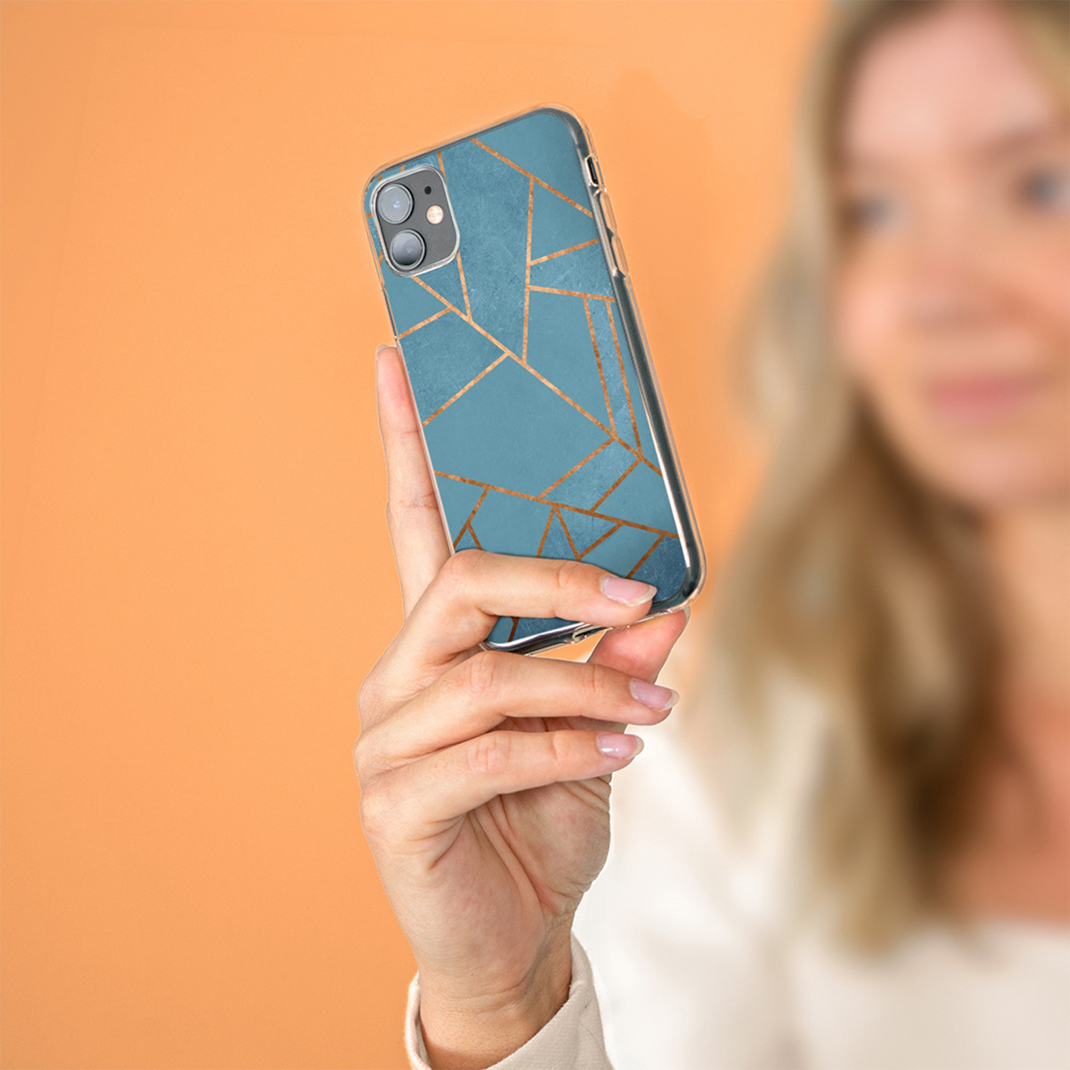 Una mano tiene un telefono blu con motivo geometrico dorato.