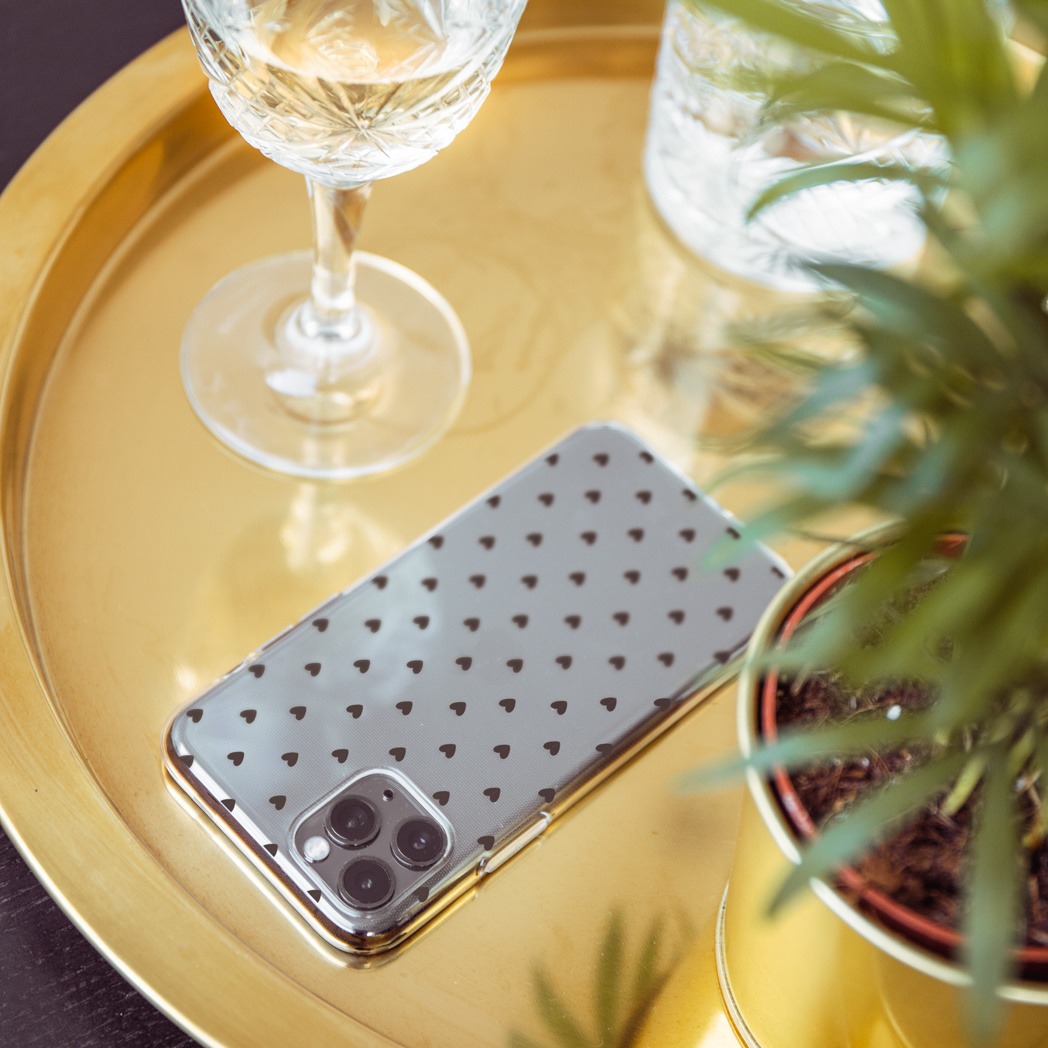 Uno smartphone con motivo a cuore su un vassoio dorato accanto a un bicchiere di vino.