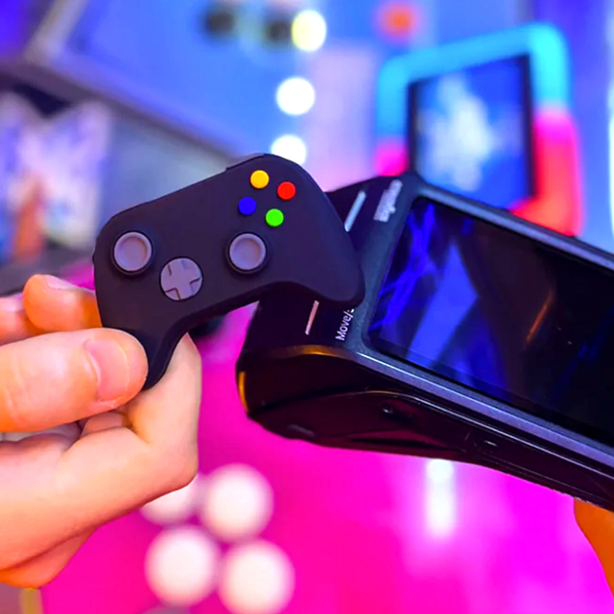 Una mano tiene un piccolo controller nero con pulsanti colorati davanti a un dispositivo.