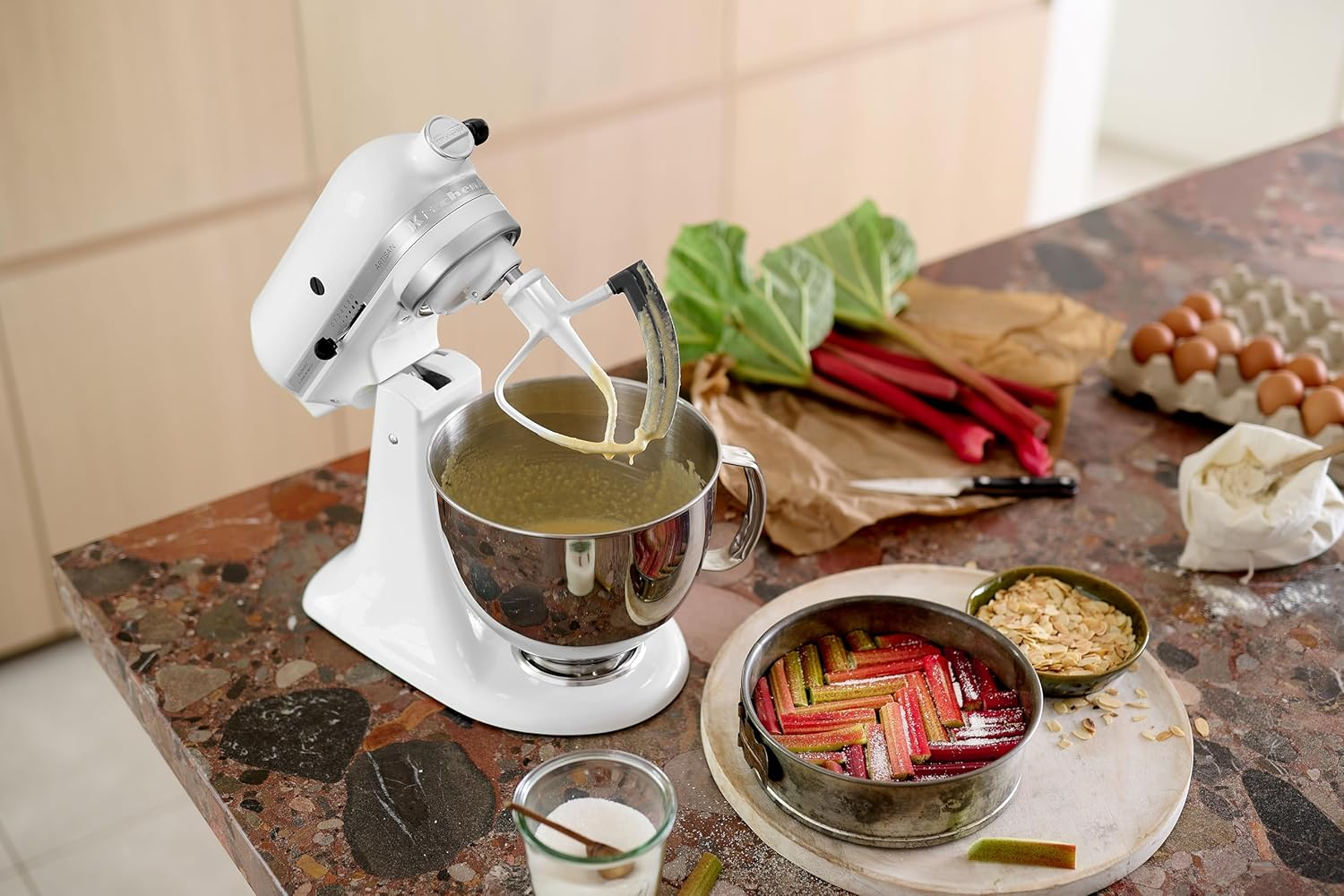 Ein weißer Standmixer mixt Teig, neben Rhabarberkuchen und Zutaten.
