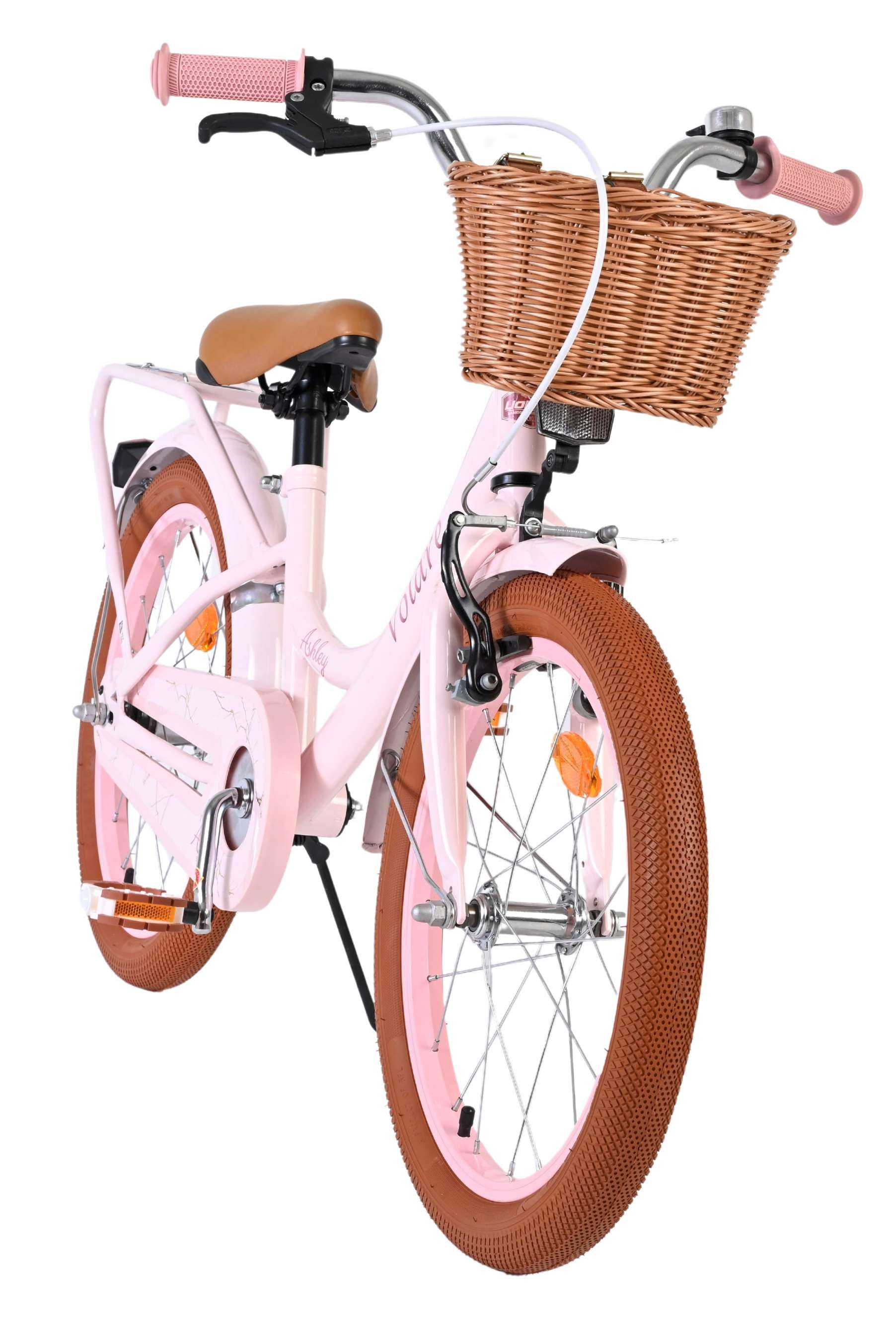 Ein rosa Kinderfahrrad mit braunen Reifen, einem geflochtenen Korb und braunem Sattel.