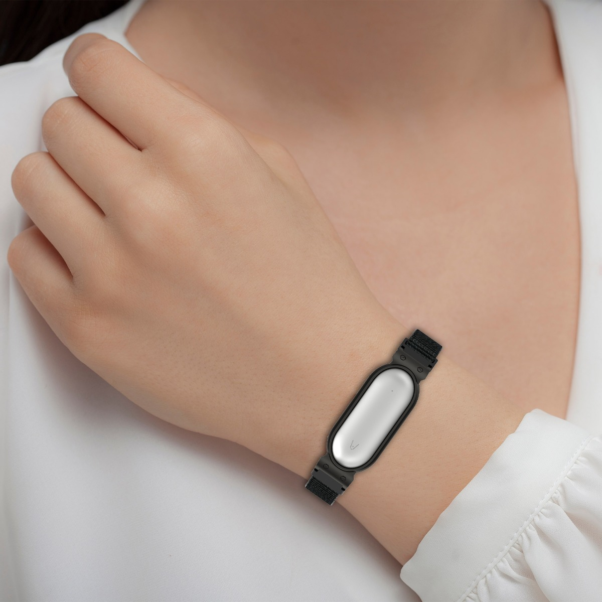 Una donna indossa una camicia bianca e un bracciale nero con display ovale argentato.