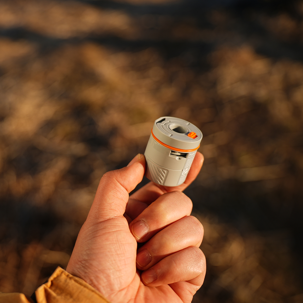 Eine Hand hält ein kleines graues und oranges Gerät mit einem orangen Knopf.