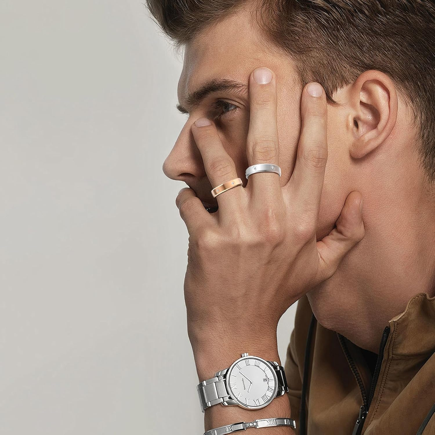 Mann mit zwei Ringen und einer Uhr, der sein Gesicht berührt.