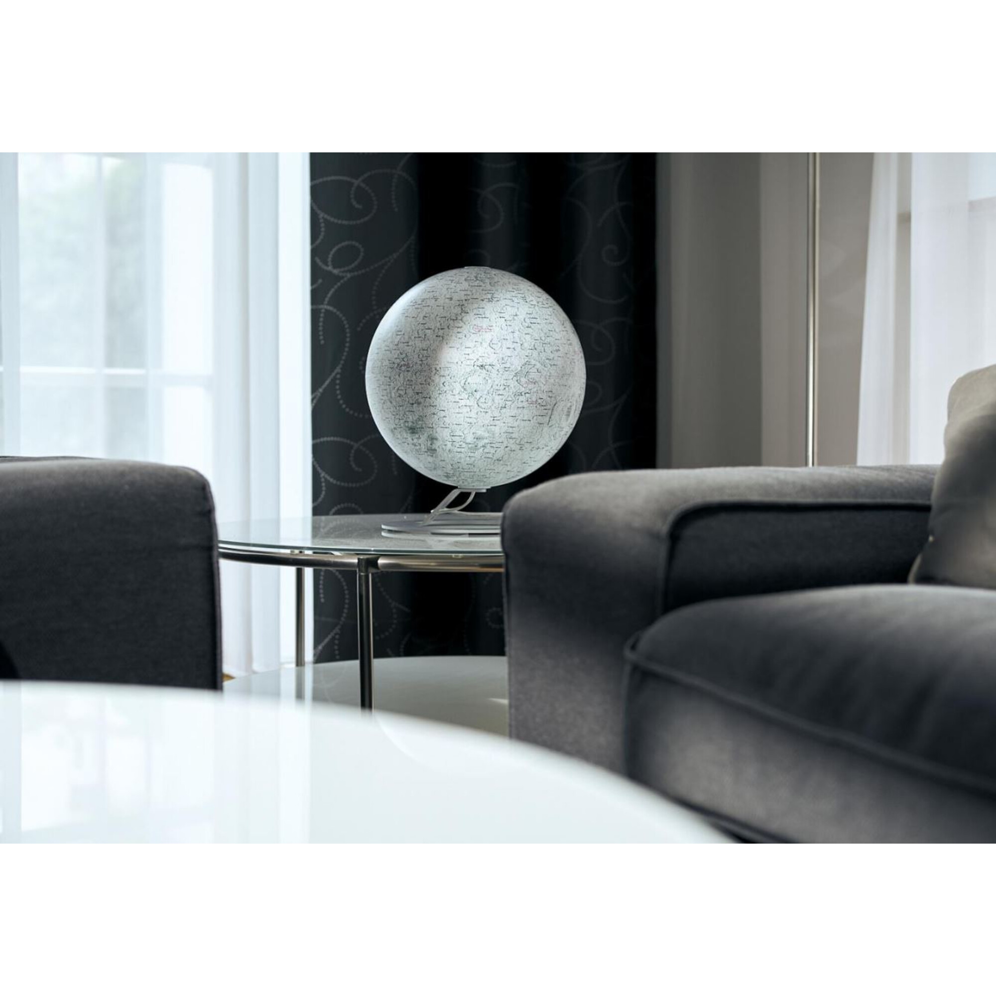 Ein weißer Globus mit Karten auf einem Glastisch zwischen zwei dunklen Sofas.
