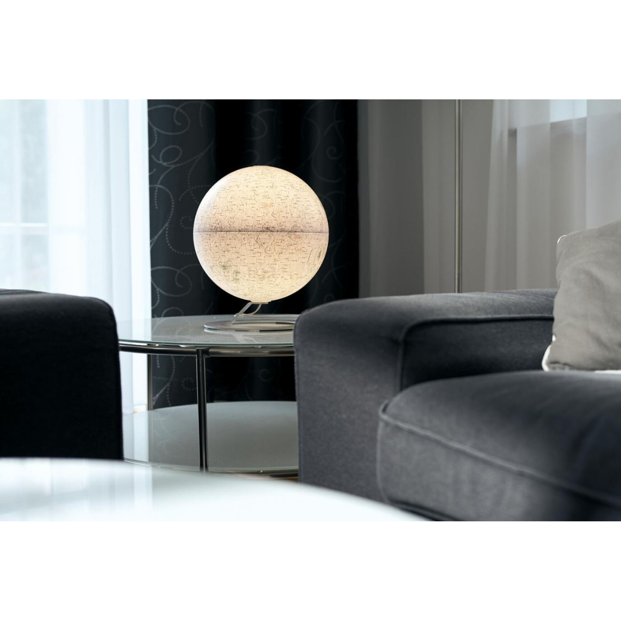 Eine beleuchtete Weltkugel steht auf einem Glastisch neben einem Sofa.