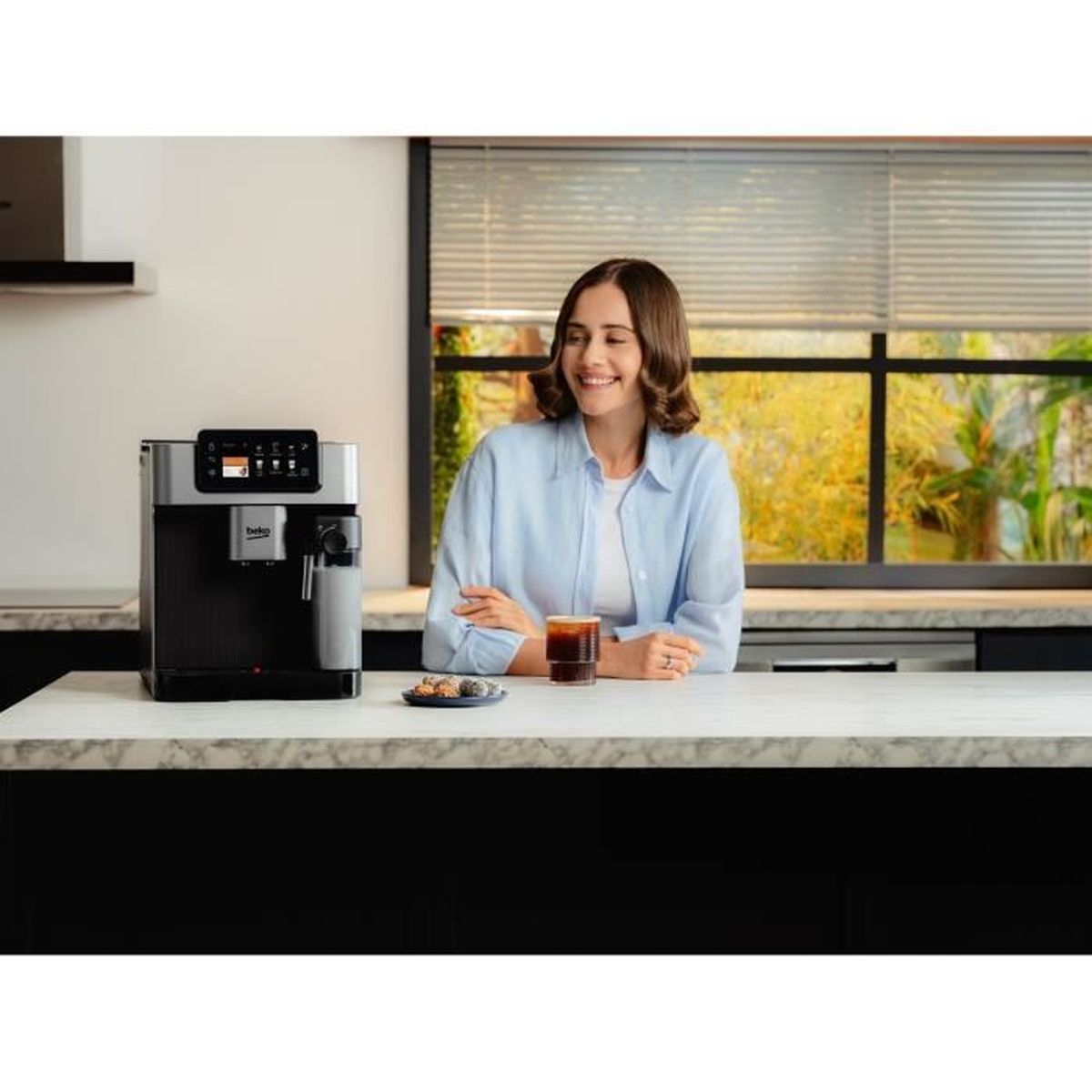 Una donna sorridente accanto a una macchina da caffè con un bicchiere di caffè.