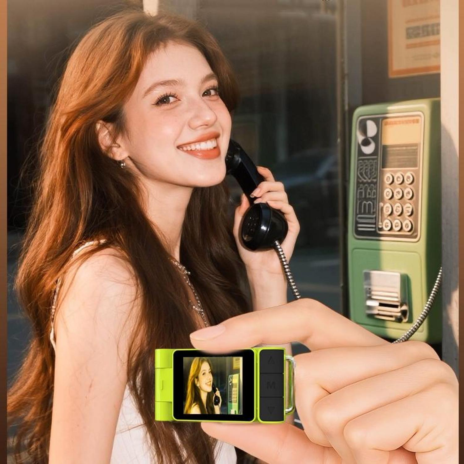 Frau telefoniert, hält Kamera, grüne Telefonzelle im Hintergrund.