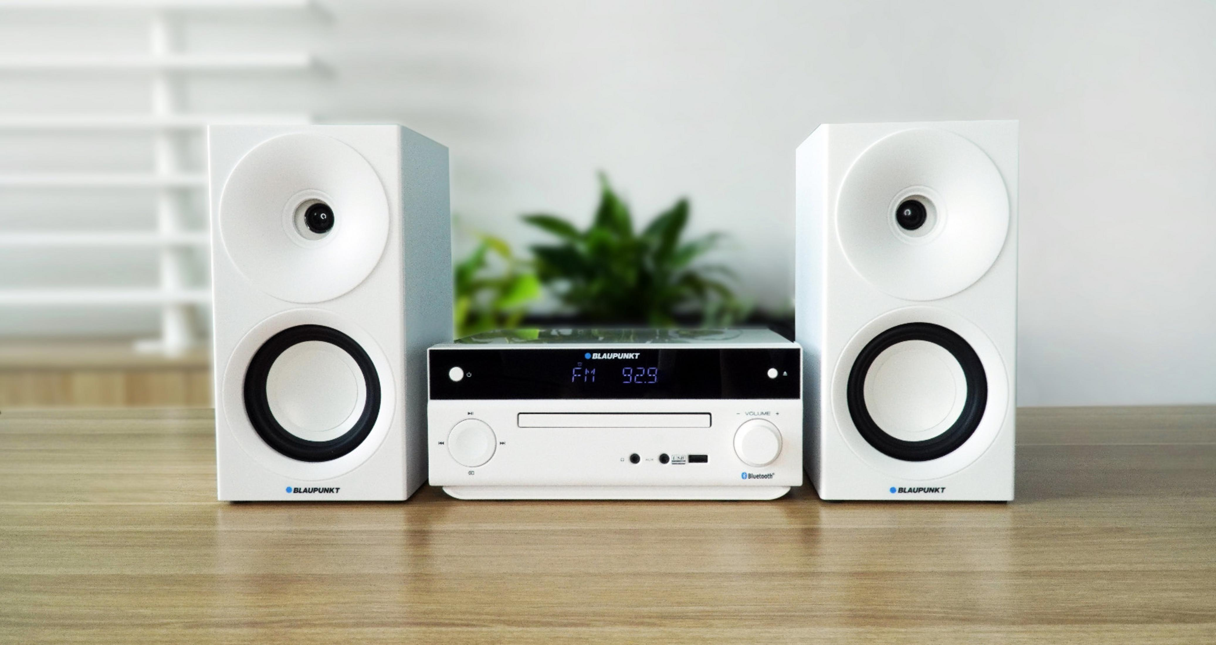 Un sistema audio bianco con lettore CD e due altoparlanti su tavolo di legno.