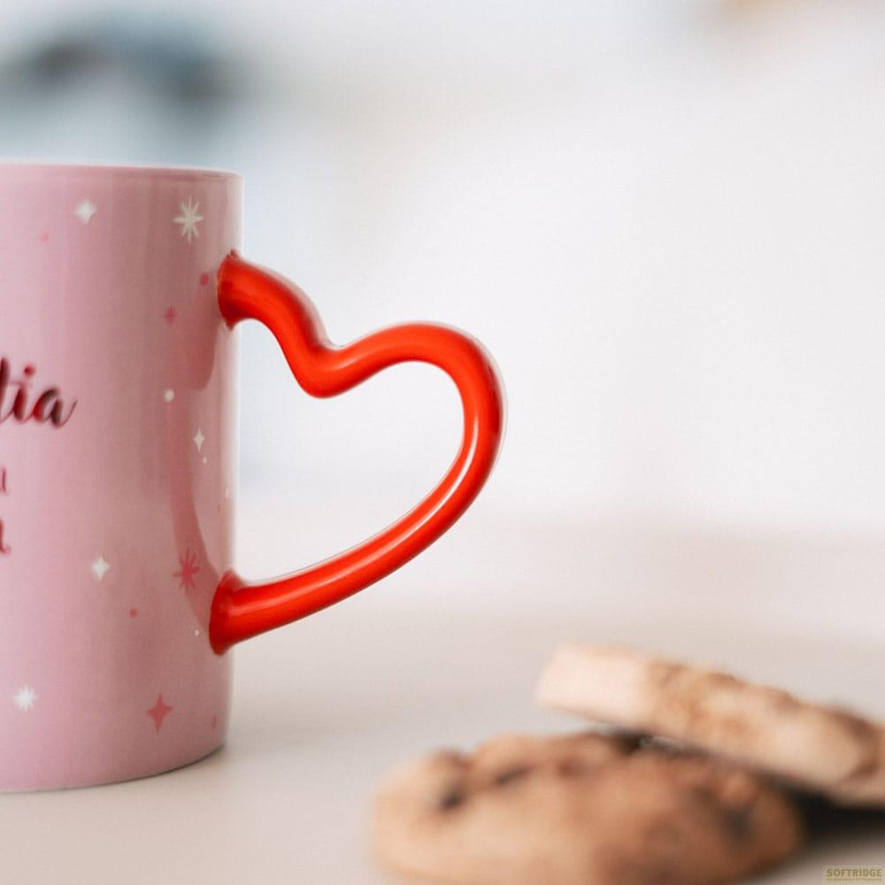 Una taza rosa con asa de corazón y galletas en primer plano.