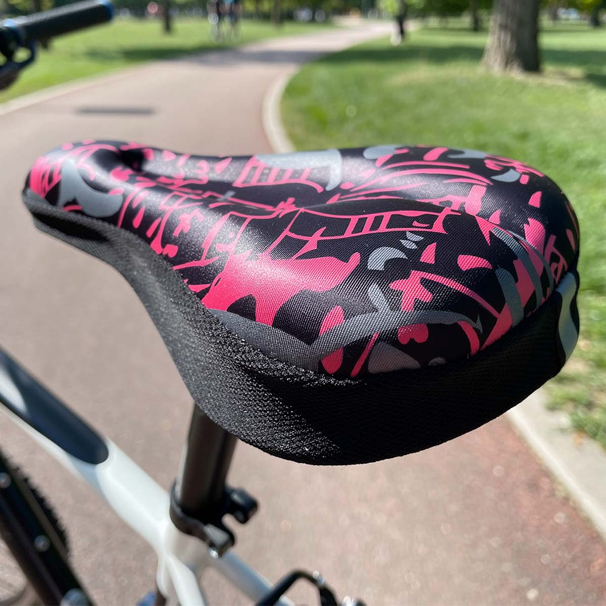 Ein pink-schwarz gemusterter Fahrradsattel auf einem Radweg im Park.
