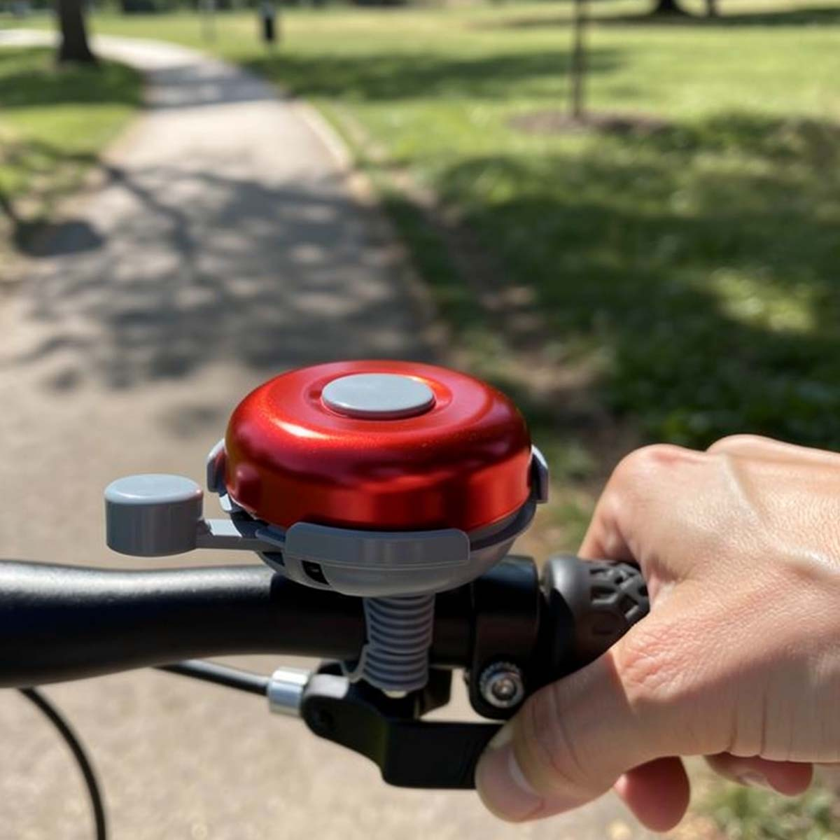 Rote Fahrradklingel am Lenker, Hand hält Griff, Weg im Park.