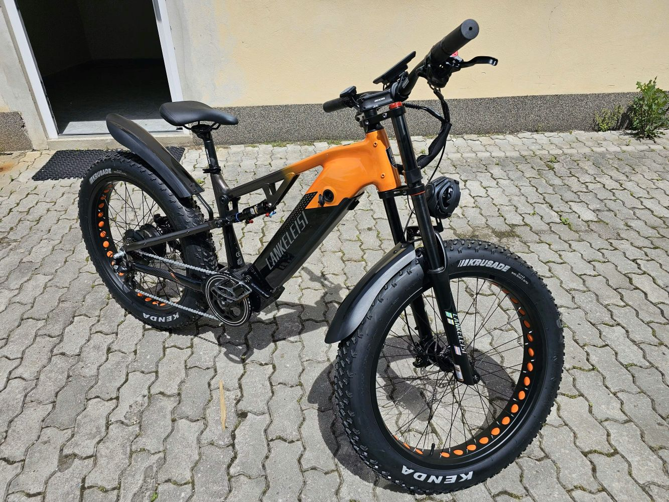 Una bicicleta eléctrica naranja y negra con ruedas anchas está en pavimento.