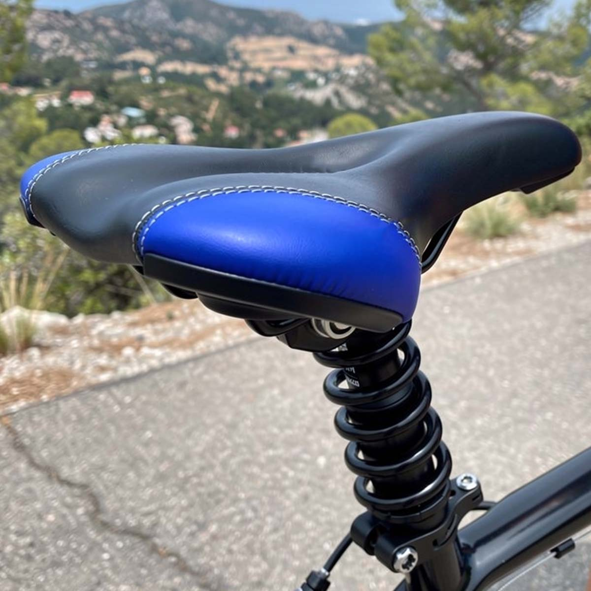 Schwarzer Fahrradsattel mit blauen Akzenten und Stoßdämpferfederung, bergige Landschaft.