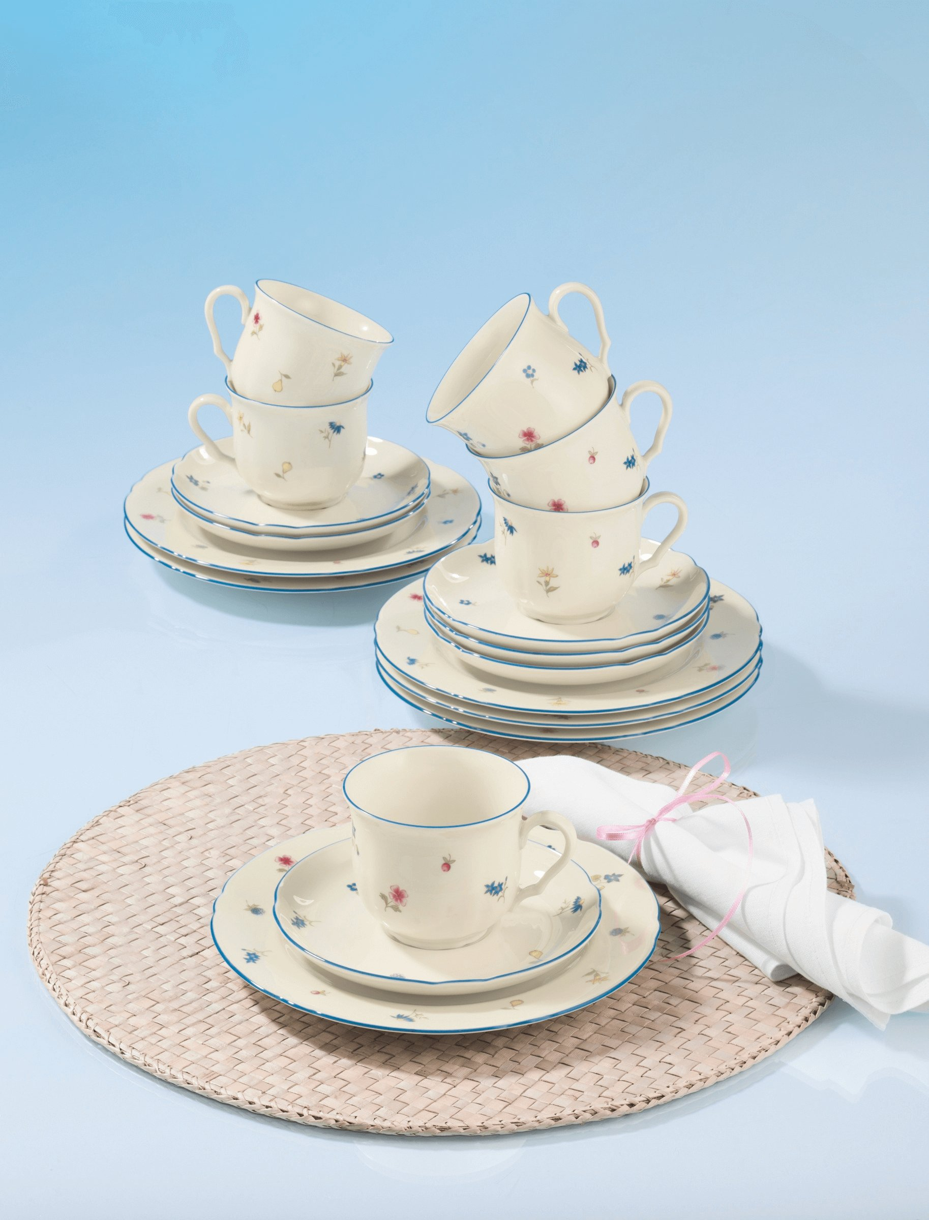 Tazzine e piattini color crema con motivo floreale e bordo blu su sfondo blu.