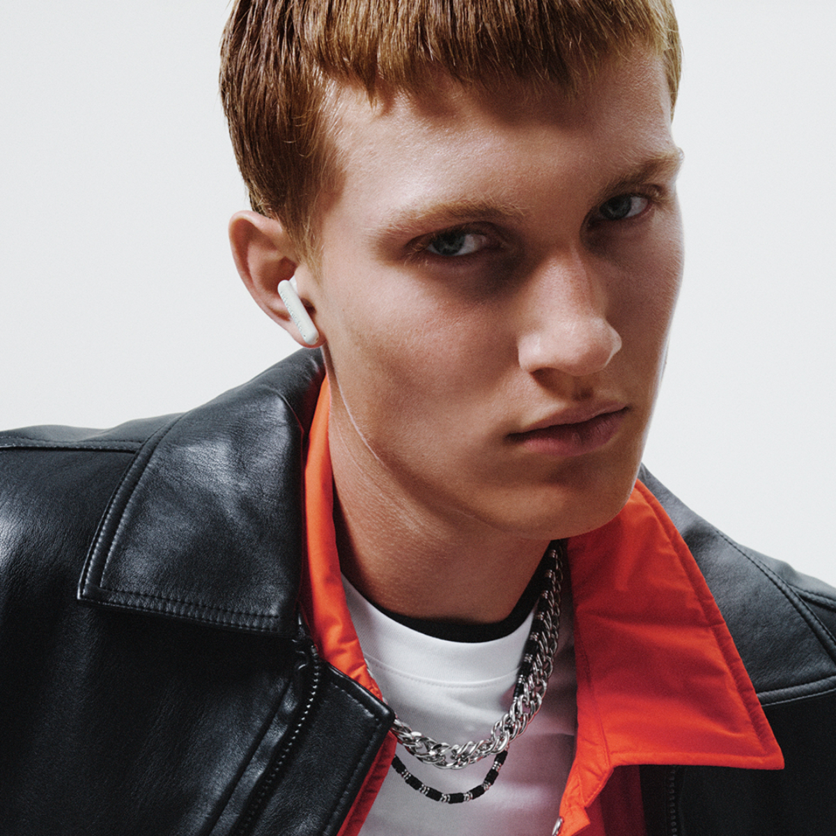 A red-haired man wears a black leather jacket and white earbuds.