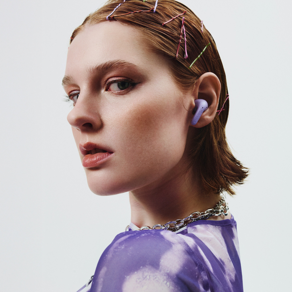 Una modella con auricolari viola e forcine tra i capelli.