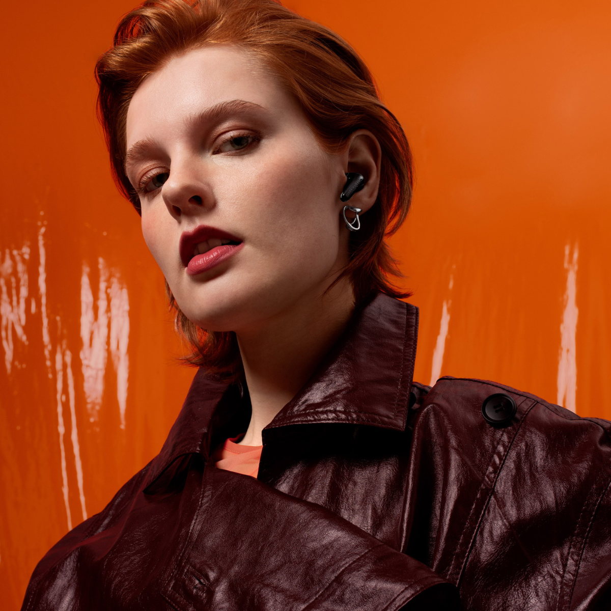 Donna con capelli rossi e giacca di pelle su sfondo arancione.