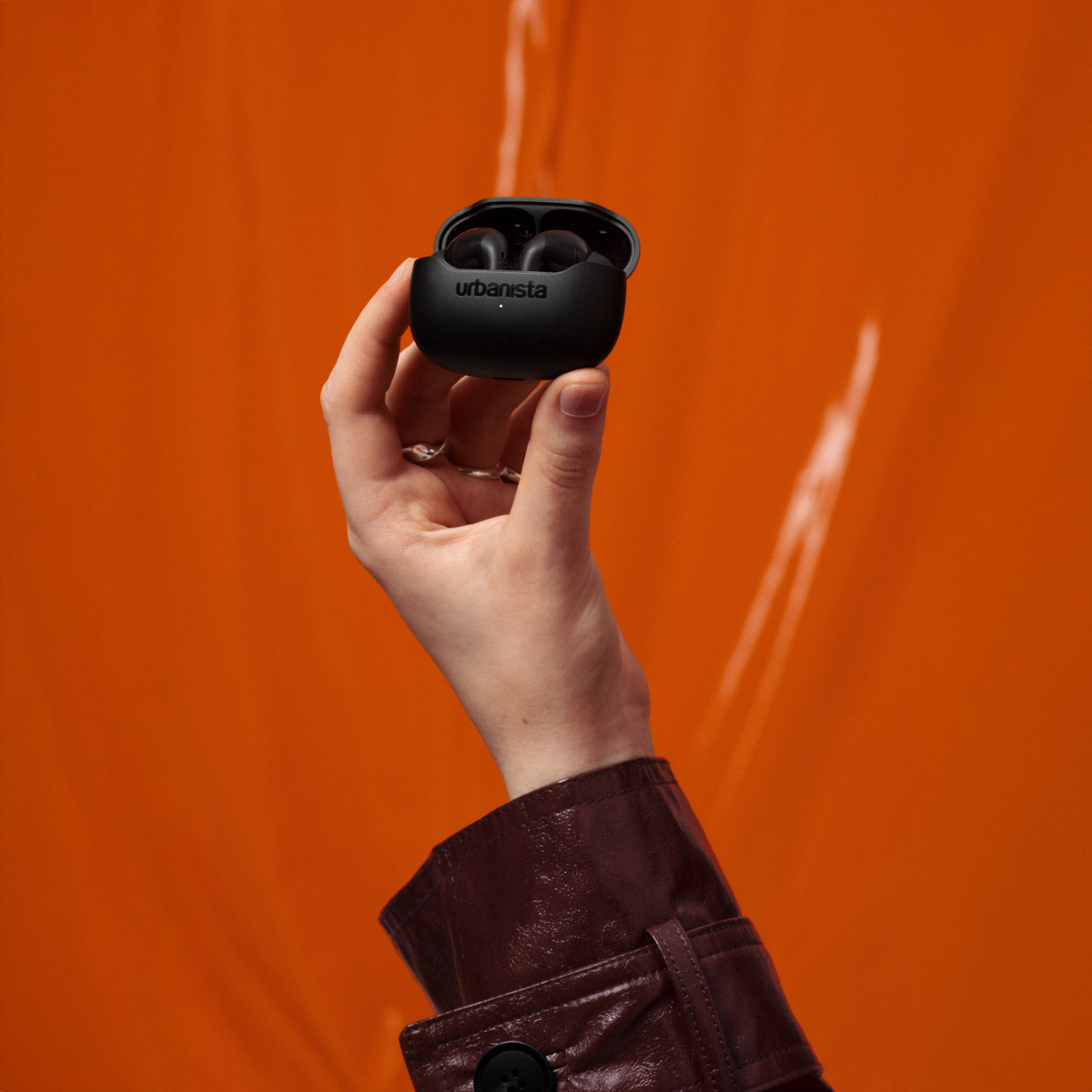 Una mano tiene una custodia di ricarica nera con auricolari su sfondo arancione.