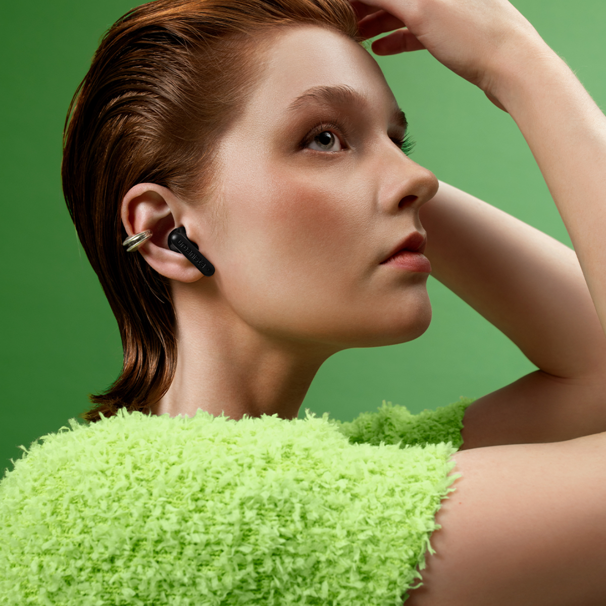 A woman with red hair wears a black earbud and a bright green top.
