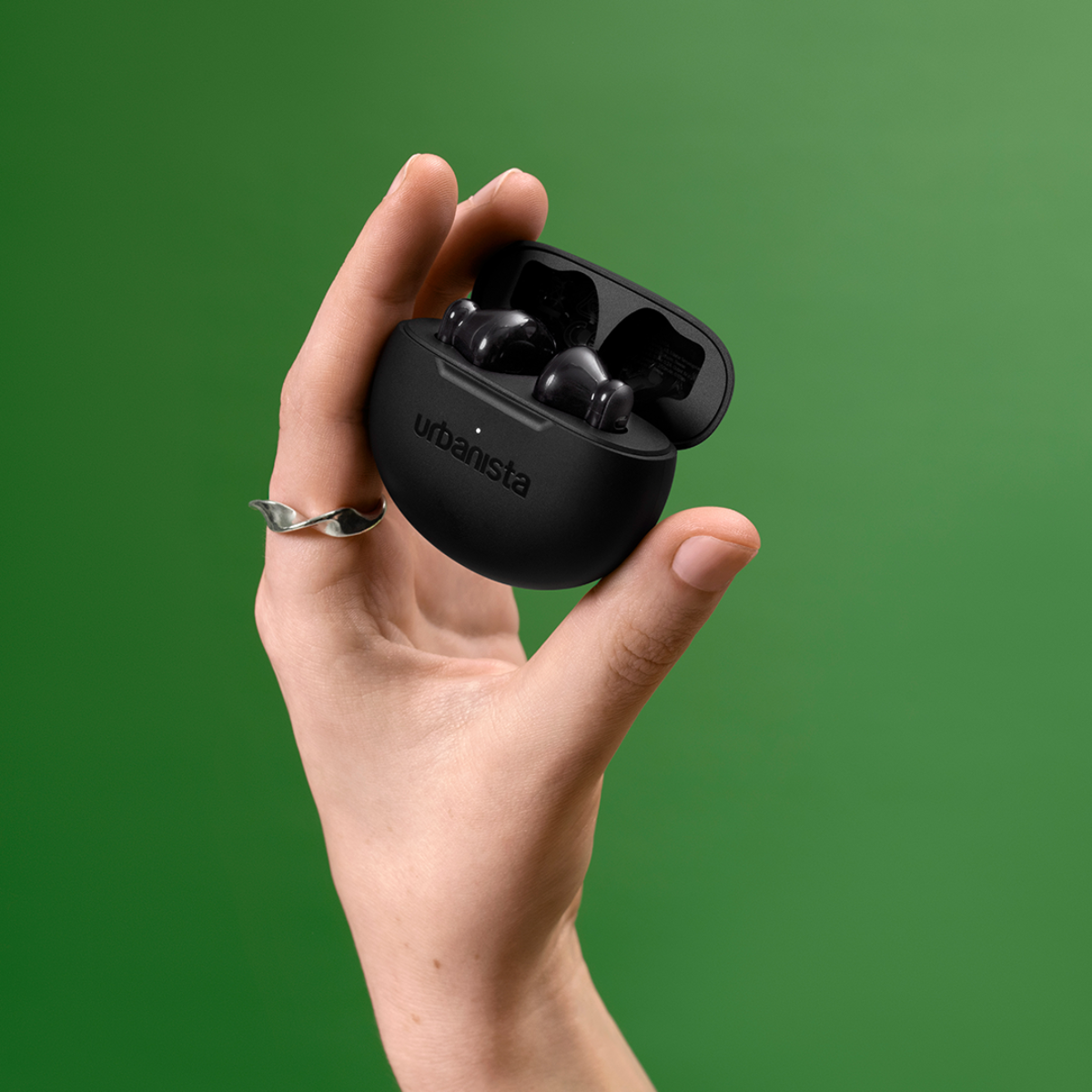 A hand holds an open black charging case with earbuds. Green background.