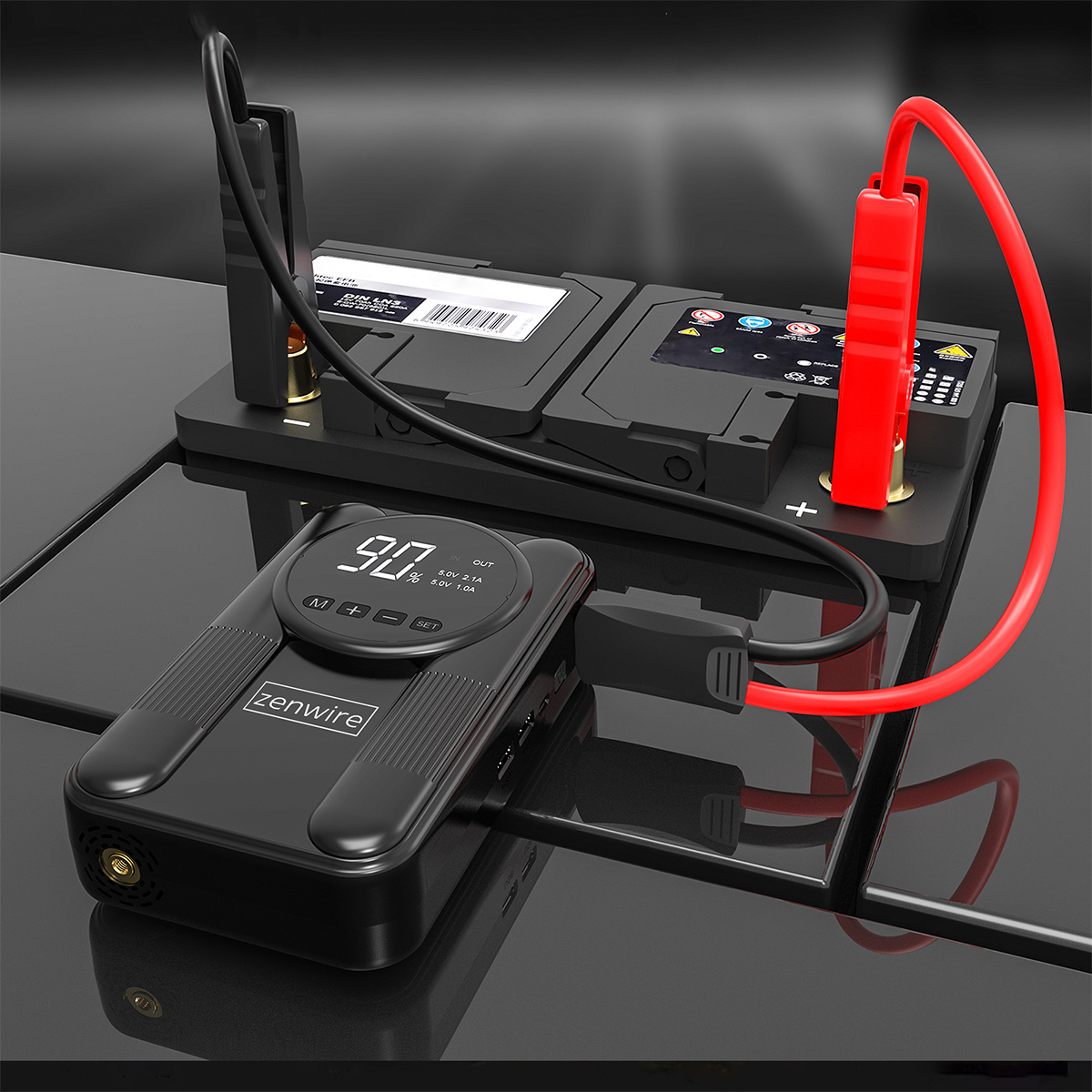 Czarny booster rozruchowy z cyfrowym wyświetlaczem podłączony do akumulatora samochodowego.