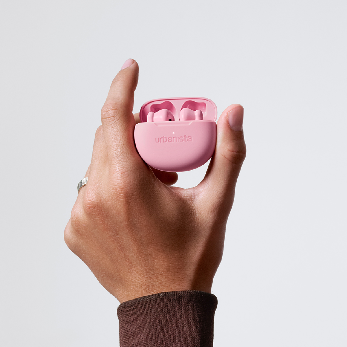 A hand holds a pink Urbanista case with its lid open, revealing two pink earbuds.