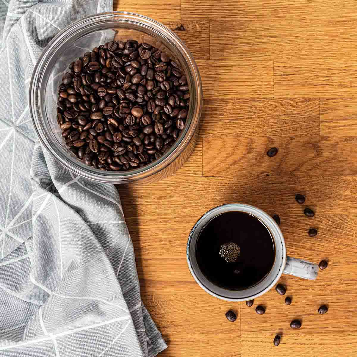 Caffè in grani in vetro, tazza di caffè su tavolo di legno, panno grigio.