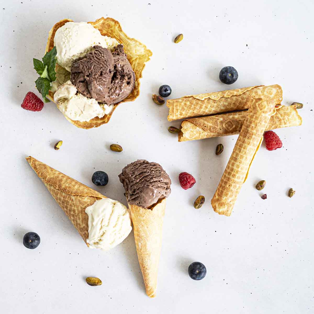 Lody w wafelkach, jagody i pistacje na białym tle.