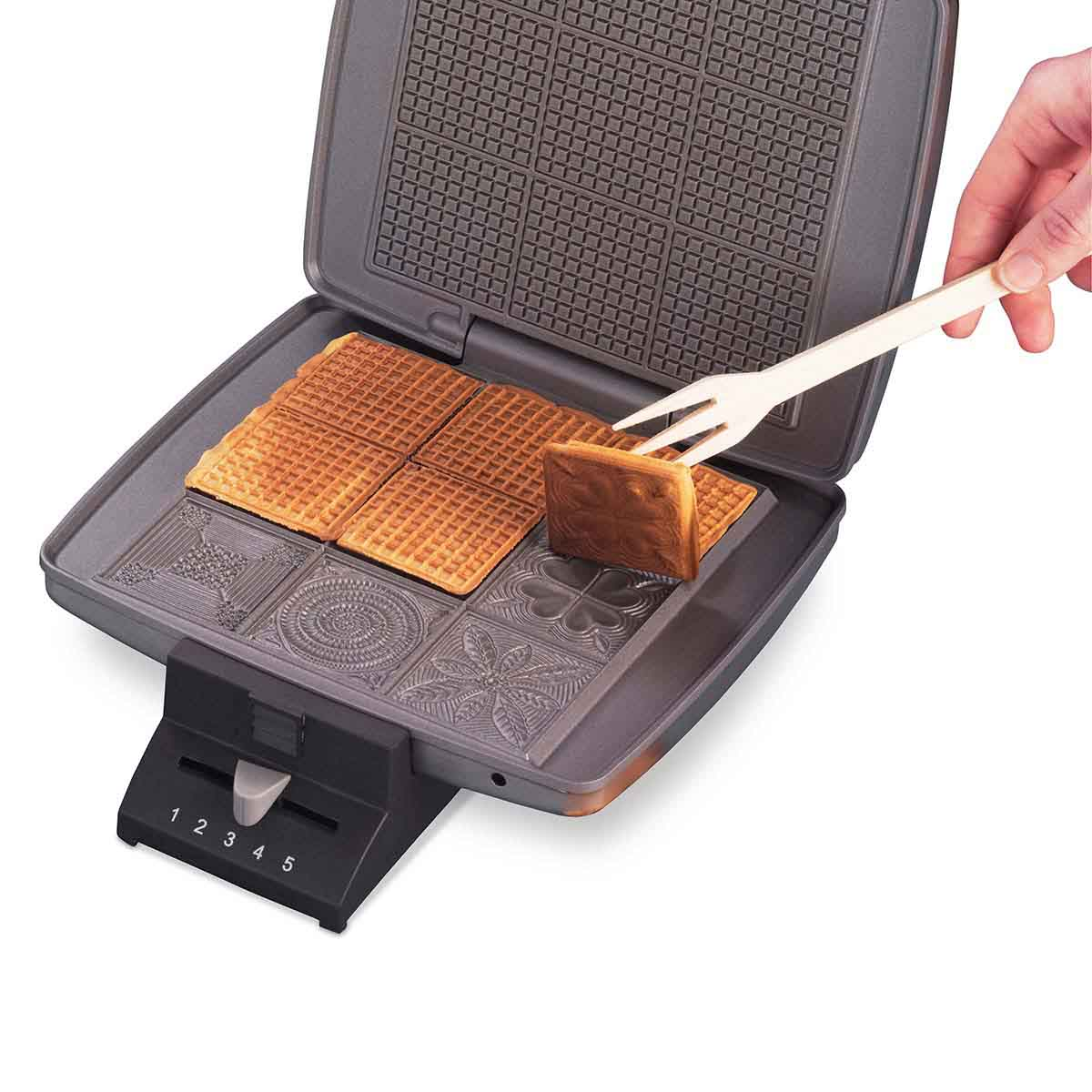 Ein Waffeleisen mit offenem Deckel, das Waffeln und eine Gabel zeigt, die eine heraushebt.