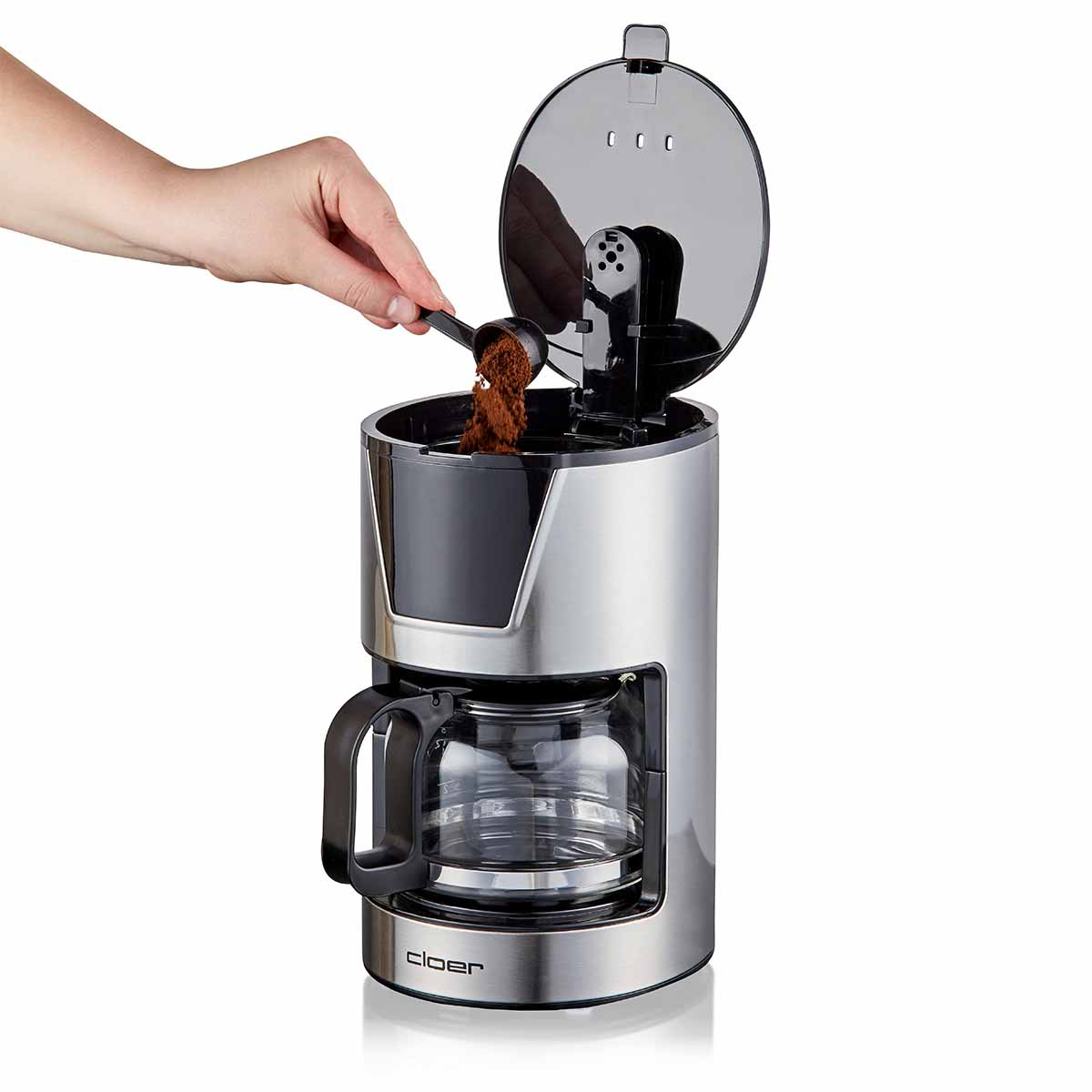 Ręka wsypuje kawę mieloną łyżką do srebrnego ekspresu do kawy.