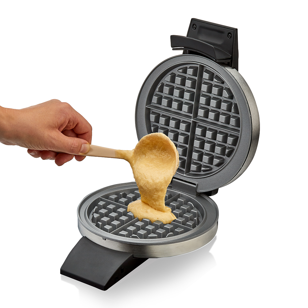 Una mano versa pastella da un cucchiaio in una piastra per waffle aperta.