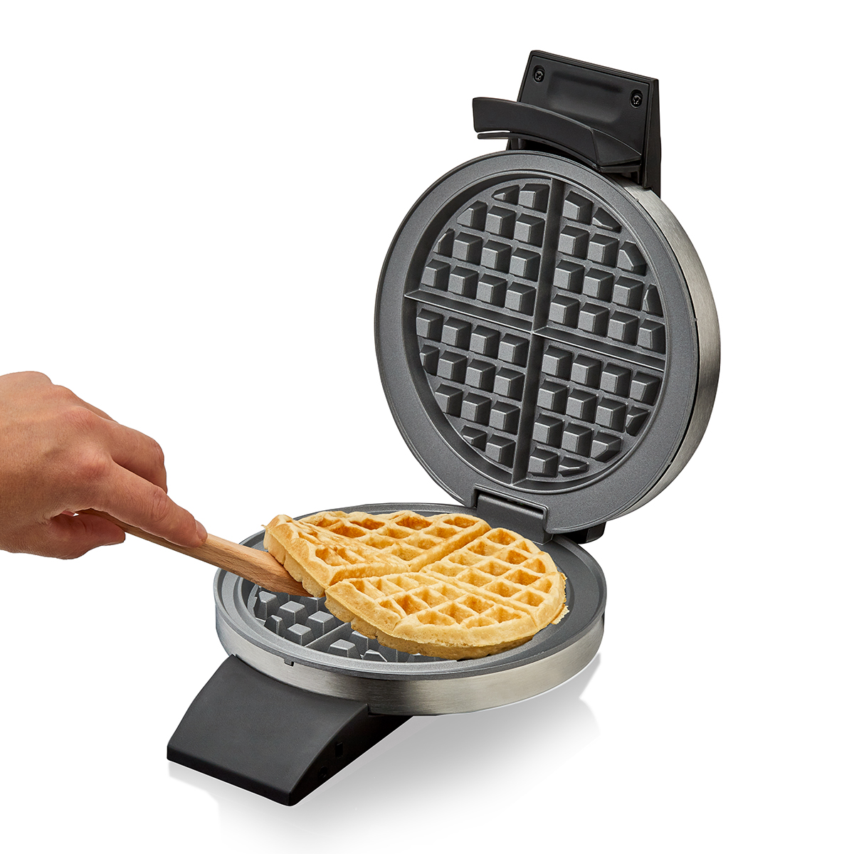 Una mano usa una spatola di legno per rimuovere un waffle dorato da una piastra per waffle aperta.