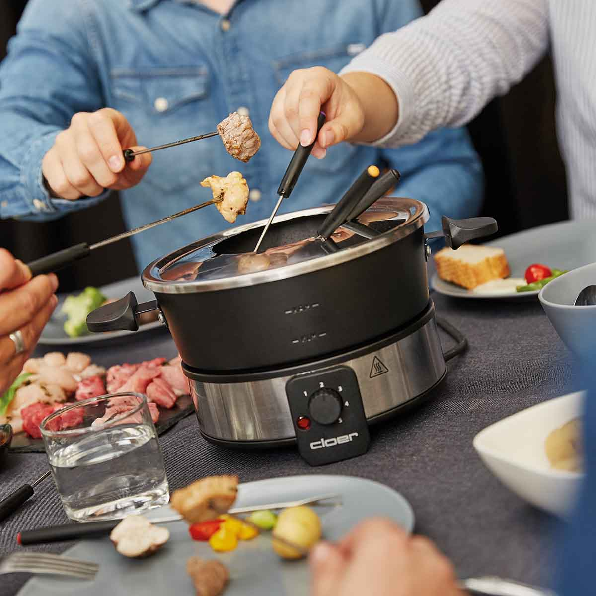 Osoby zanurzają mięso i chleb w garnku do fondue z gorącym płynem.