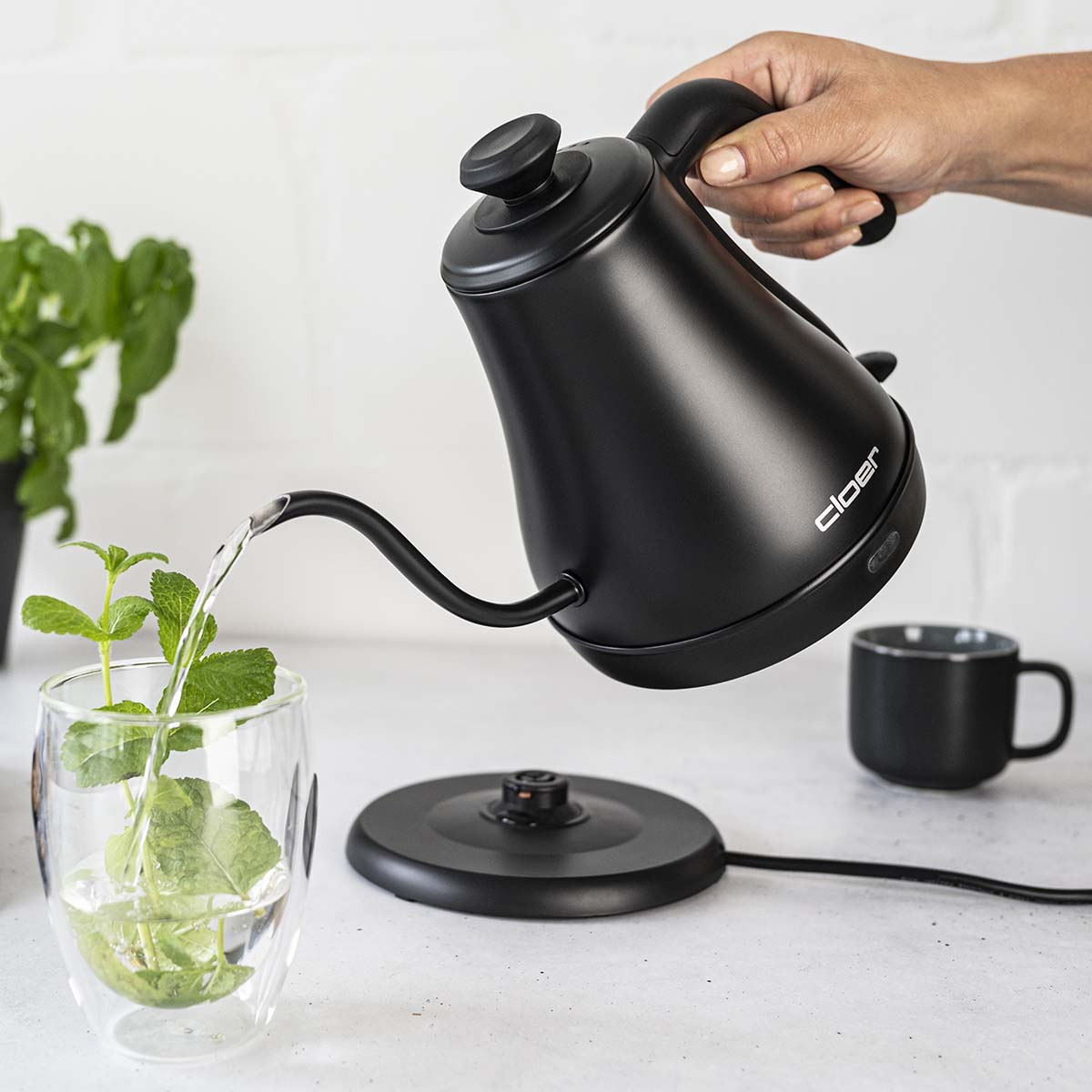 Eine schwarze Elektrokanne gießt heißes Wasser in ein Glas mit Minze.