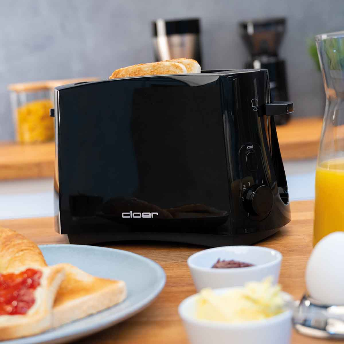 Schwarzer Toaster mit Toast, Orangensaft, Ei und Brot auf dem Tisch.