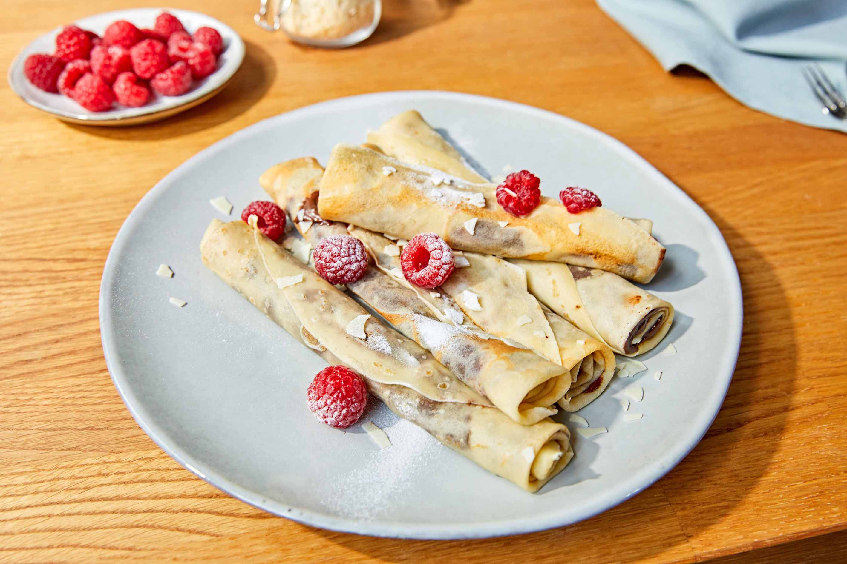 Crepes arrotolate con lamponi e zucchero a velo su un piatto.