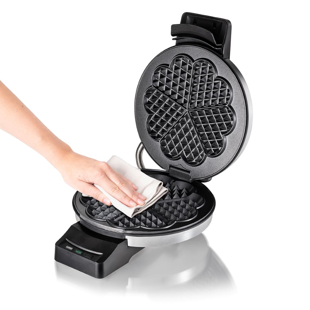 Dłoń wyciera płytę grzewczą otwartej gofrownicy ściereczką.