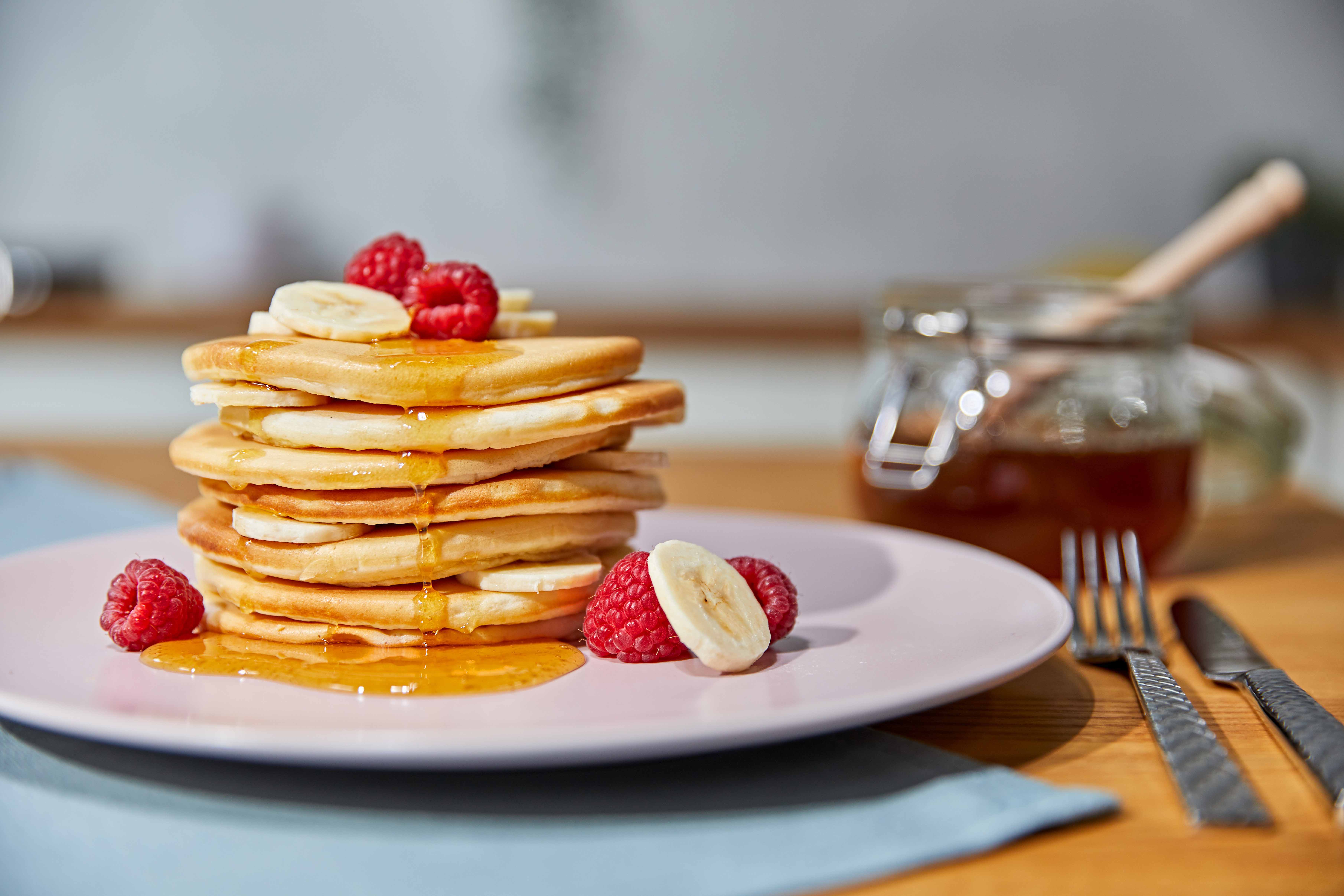 Una pila di pancake con pezzi di banana e lampone, irrorati di miele.