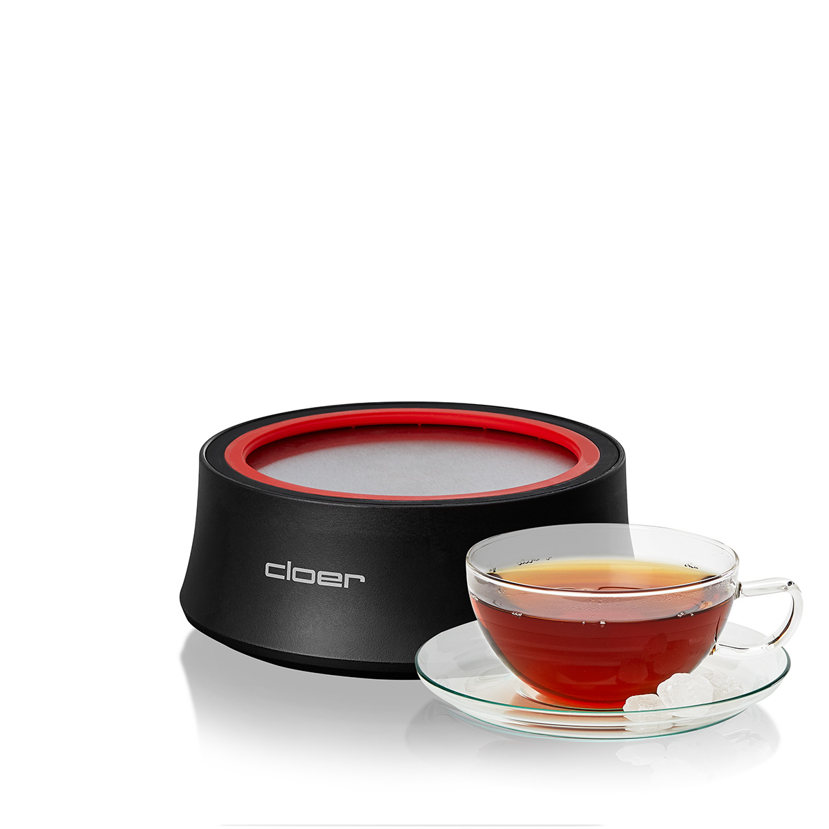 Ein schwarzer Teewärmer mit rotem Rand neben einer Teetasse mit Tee und Zuckerwürfeln.