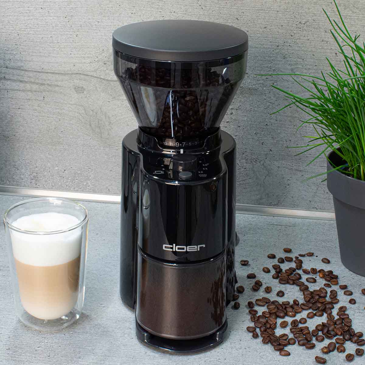 Schwarzer Kaffeemühle mit Bohnenbehälter, daneben ein Glas Latte Macchiato.